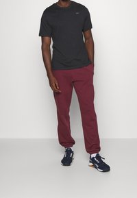 Outfit da uomo che include una t-shirt nera a maniche corte, pantaloni sportivi bordeaux e sneakers blu navale con dettagli bianchi. Design semplice, stile casual.