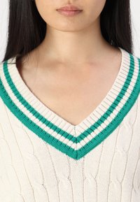 Suéter de punto en crema con un profundo escote en V y acentos acanalados a rayas en azul verdoso en el cuello. Tejido texturizado y sensación ligera.