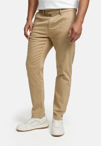 Chinos kaki à coupe droite, confectionnés dans un tissu lisse. Dotés de poches latérales, poches arrière et d'un passants pour ceinture, associés à des baskets blanches.