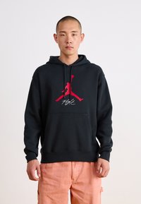 Hanorac negru din material moale, având un logo roșu Air Jordan și textul "Flight", cu un buzunar frontal și glugă cu șnur reglabil.