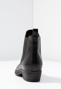 Bottines en cuir noir avec une finition texturée, des panneaux latéraux élastiques et un petit talon empilé. Elles sont dotées d'une languette à l'arrière.