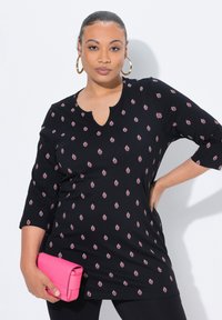 Tunic nera con motivo a foglie rosa, scollatura rotonda e maniche a tre quarti. Abbinata a una pochette rosa. Tessuto liscio.