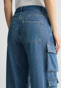 Tumed sinised denim cargo püksid valgete pärliga kaunistusega, kahe tagatasku ja küljetaskuga.