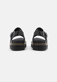 Sandali in pelle nera con fibbia regolabile, design aperto sul retro, suola in gomma spessa e cuciture gialle a contrasto lungo il bordo.