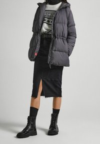 Šedá prošívaná bunda s kapucí, černý svetr s bílým a šedým vzorem, černá džínová sukně s předním rozparkem a černé kotníkové boty na šněrování.