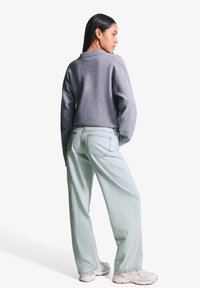 Sivi skraćeni pulover, svijetloplave traperice i bijele tenisice. Pulover ima okrugli izrez i ležeran kroj. Traperice imaju džepove i široku siluetu.