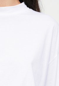 Λευκό κοντομάνικο μπλουζάκι από απαλό βαμβακερό ύφασμα με ψηλό στρογγυλό λαιμόκομμα και χαλαρή εφαρμογή, με λεία υφή και χωρίς ορατά μοτίβα.