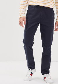 Mörkblå chinos av bomull med en slät yta, med klassisk passform och framfickor, i kombination med vita sneakers med röda accenter.