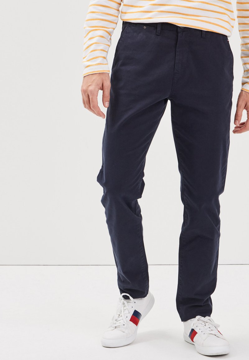 Mörkblå chinos av bomull med en slät yta, med klassisk passform och framfickor, i kombination med vita sneakers med röda accenter.