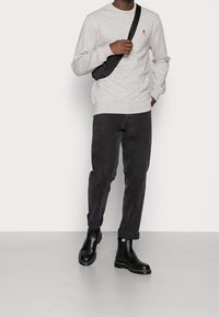 Szary polarowy sweter z małym kolorowym logo, zestawiony z czarnymi spodniami z kordurowej tkaniny i czarnymi elastycznymi botkami za kostkę. Nosi małą czarną torebkę na ramię.