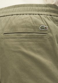 Shorts vert olive en tissu lisse, dotés d'une poche arrière à la finition soignée et d'un logo crocodile brodé dans un coin.