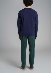 Una camicia a maniche lunghe blu navy abbinata a pantaloni a scacchi verdi, con una vestibilità comoda e materiale in cotone morbido, vista da dietro.