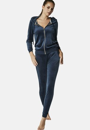Ensemble de survêtement en velours bleu marine comprenant un sweat à capuche zippé avec poches et un pantalon fuselé assorti. Texture lisse avec des poignets côtelés.