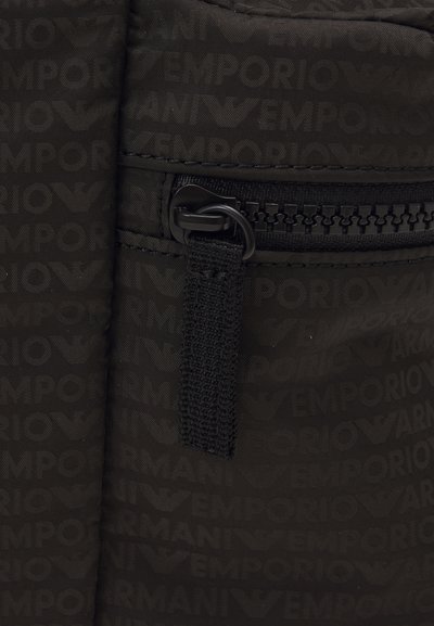 Svart tygväska med ett zip-fack, präglad logotyp och en strukturerad rem för enkel hantering.