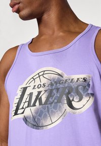 Débardeur violet avec un grand logo en relief des Los Angeles Lakers et un graphique de basketball. Matière en coton lisse avec un col rond.