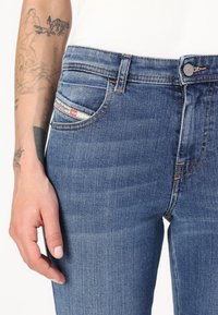 Vaqueros de mezclilla azul con una cintura de altura media, que presentan un diseño clásico de cinco bolsillos, costuras sutiles y una etiqueta de marca en el bolsillo delantero.