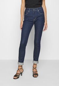 Mörkblå jeans med slim fit, mid-rise midja och uppvikta fållar, tillsammans med svarta remsandaler med hög klack.