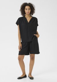 Schwarzes Leinenoberteil mit kurzen Ärmeln und V-Ausschnitt, kombiniert mit schwarzen Shorts, die zwei Fronttaschen haben, eine glatte Textur und eine lockere Passform aufweisen.