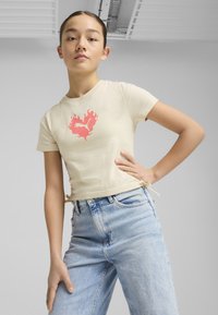 Camiseta beige con un diseño gráfico de llamas rosas en el centro, combinada con unos pantalones vaqueros de denim azul claro de cintura alta, con lazos laterales.