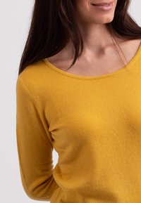 Gelber Strickpullover mit Rundhalsausschnitt und langen Ärmeln, der eine weiche Textur und eine entspannte Passform aufweist.