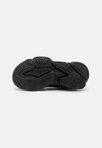 Black sneaker sole with curved, textured patterns. Features rounded sections and various grip points for improved traction. Rubber material.