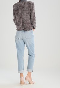 Blazer texturé multicolore à la coupe structurée, associé à un jean bleu clair retroussé et des escarpins nude. Vue arrière de la tenue.