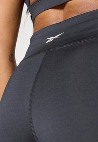Leggings atletici neri a vita alta con tessuto liscio, presentano un logo bianco sulla vita e cuciture rinforzate per una maggiore durabilità.