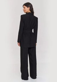 Czarna dopasowana marynarka z paskiem w talii oraz spodniami o szerokich nogawkach; charakteryzuje się usztywnionym kołnierzem i gładką teksturą materiału.