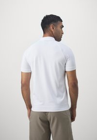 White short-sleeve polo shirt with a collared neckline, made from a smooth fabric. Features raglan sleeves and a straight hem.