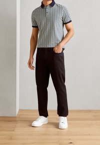 Polo à col bleu marine et blanc avec un motif, associé à un jean noir et des baskets blanches. Le polo présente des manches courtes et un design texturé.