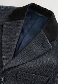 Szürke houndstooth mintás blézer, corduroy gallérral. Belső része sötétkék mintás béléssel rendelkezik. Egy gomb és egy zsebbel.