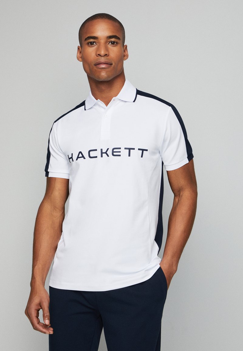 Polo shirt bianco con accenti blu navy sulle spalle e grande scritta "HACKETT" sul petto. Tessuto morbido e design del colletto classico.