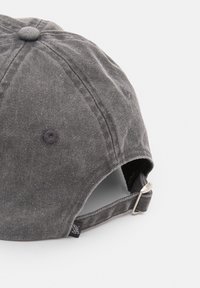 Grå bomullsmössa med en sydd toppknapp, justerbar rem bak och subtilt texturerad tyg med liten märkesetikett.