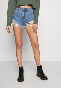 Denim shorts in light blue, with frayed hems and distressing. Paired with black lace-up boots. Background is plain gray.