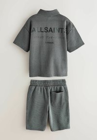 Sivý textúrovaný top s krátkym rukávom a golierom a zodpovedajúce elastické šortky s pásom, oba s logom "ALLSAINTS" a japonským textom na tope.