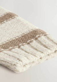 Couverture en laine crème et beige avec un motif rayé. Elle présente une texture douce et des franges sur un bord.