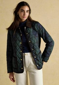 Jachetă matlasată de culoare verde închis, cu guler din catifea călduroasă maro. Are nasturi aurii, buzunare laterale și un logo brodat pe piept.