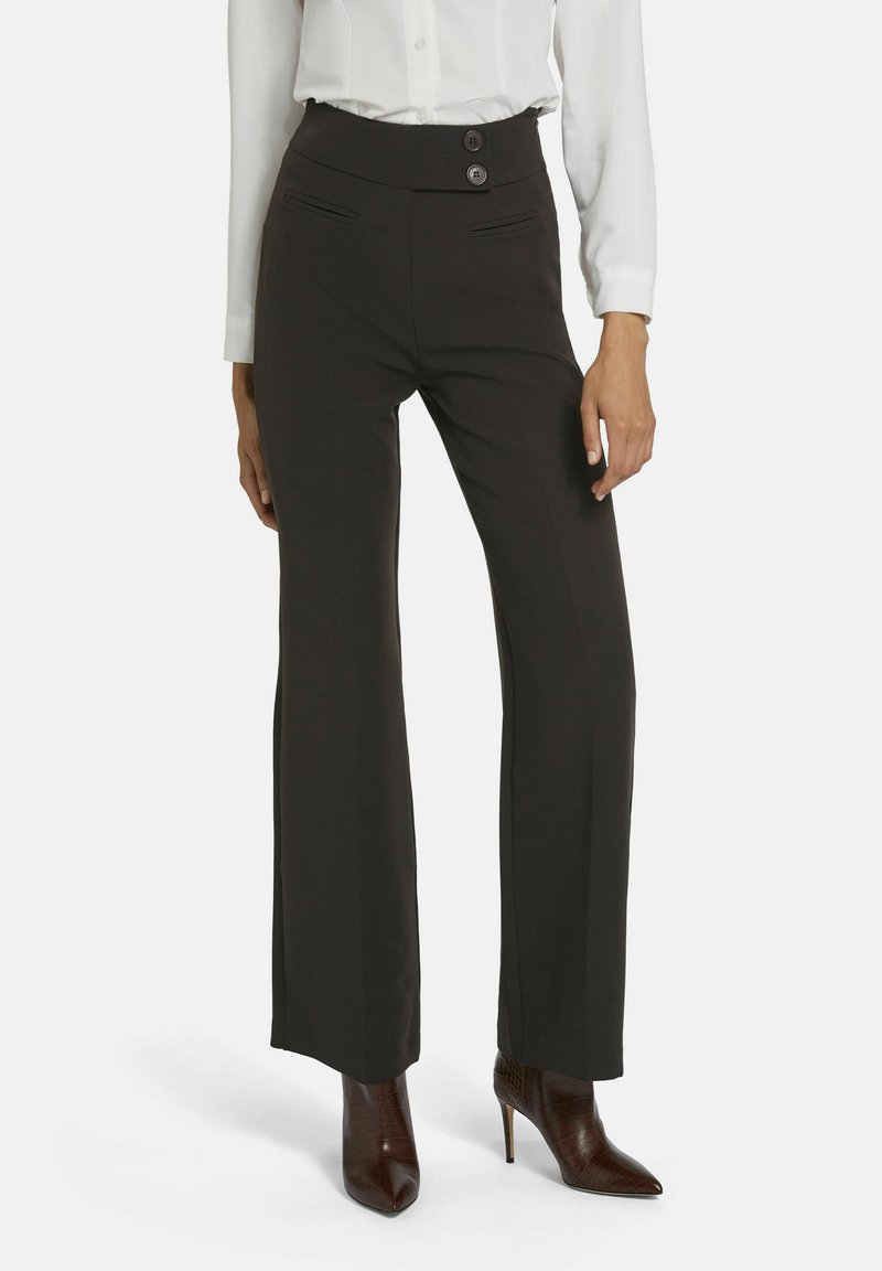 Zwarte wijde broek met hoge taille, twee knopen en zijzakken. Draagt met puntige bruine hoge laarzen. Glad stoftextuur.