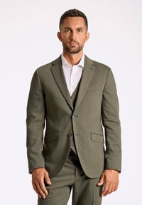 Olijfgroen pak met een notch lapel, een enkelvoudige blazer en bijpassende broeken. Witte overhemd eronder, textiel met textuur.