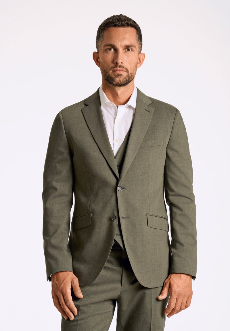 Olijfgroen pak met een notch lapel, een enkelvoudige blazer en bijpassende broeken. Witte overhemd eronder, textiel met textuur.