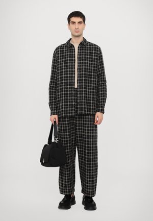 Schwarzes und cremefarbenes kariertes Hemd- und Hosen-Set, strukturierter Stoff, lange Ärmel, kombiniert mit einer schwarzen Tasche und klobigen schwarzen Schuhen.