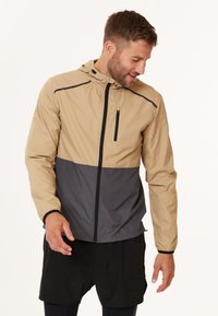 Leichte, zweifarbige Jacke mit einem oberen Abschnitt in Beige und einem unteren Abschnitt in Dunkelgrau. Sie verfügt über eine mit Reißverschluss verschließbare Vordertasche und eine Kapuze. Glattes, wasserabweisendes Material.