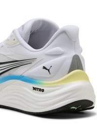 Hvid sportsko med en struktureret tekstiloverdel, sorte accenter, en bølget sål og en gradient hæl i blå og gul. Har Puma-logo.