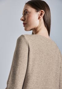 Maglione beige con trama strutturata, caratterizzato da costine verticali, una scollatura ampia e una silhouette morbida, mostrato da un'angolazione laterale.