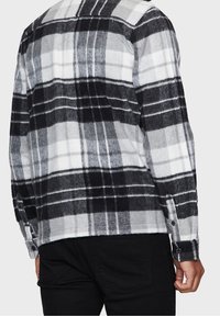 Camicia di flanella a quadretti nera, bianca e grigia. Presenta un polsino con bottoni e una vestibilità comoda con una texture morbida.