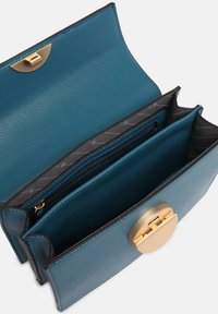 Portefeuille en cuir sarcelle avec un fermoir circulaire doré, plusieurs compartiments et un intérieur texturé avec une doublure à motifs.