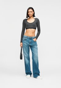 Γκρι μακρυμάνικο cropped τοπ με στρογγυλή λαιμόκοψη και λωρίδα με λογότυπο. Ανοιχτό μπλε φαρδιά τζιν παντελόνια με μπροστινές τσέπες και άνετη εφαρμογή.