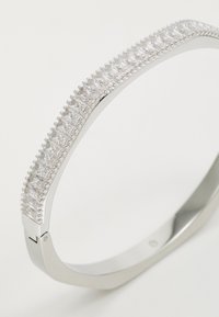 Zilveren metalen armband met een rij heldere, rechthoekige rhinestones langs de buitenrand; gladde oppervlakte met een gepolijste afwerking.