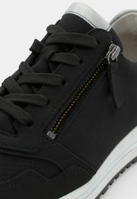 Black leather sneaker with black laces, silver zipper detail, and white sole. Features perforated accents on the upper for texture.