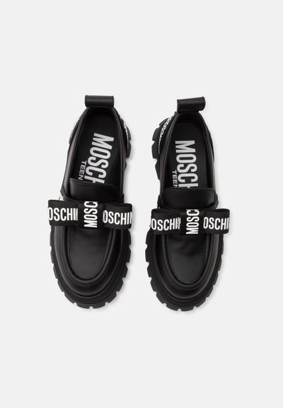 Ζευγάρι μαύρα chunky loafers με χοντρές σόλες και μαύρα λουράκια με λευκή επιγραφή "Moschino" στο μπροστινό μέρος.